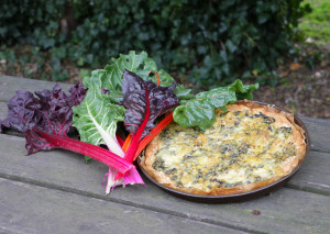 Une tarte aux blettes ainsi qu'un bouquet de blettes sont posés sur une table en bois